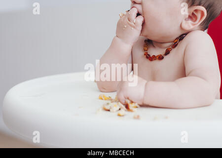 Close crop of 6 month old baby boy feeding himself in a high chair Stock Photo