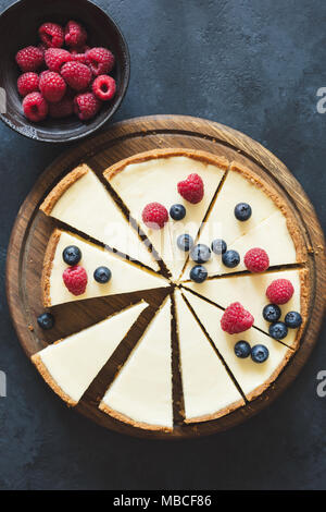 Classical cheesecake with fresh berries on wooden board cut into slices. Top view with copy space for text. Toned image Stock Photo