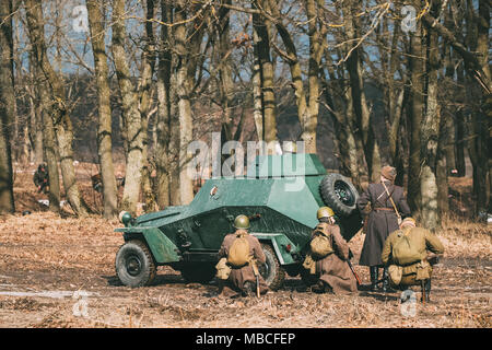 Group Of Reenactors Dressed As Russian Soviet Red Army Soldiers Of World War II Go On Offensive Under Cover Of Armored Soviet Scout Car Ba-64. Histori Stock Photo