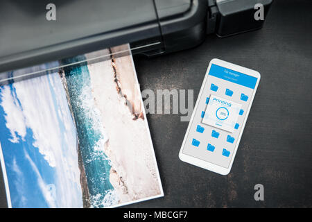 Smartphone connected to the wireless printer is laying on the desk Stock Photo