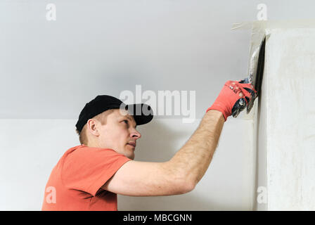 The worker puts f inishing layer of stucco on the wall using a spatula Stock Photo