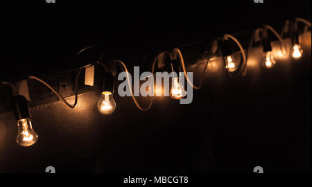 Vintage tungsten bulb lamps garland hanging on dark wall at night. Close up phtot with selective focus Stock Photo