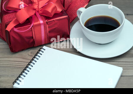 Red gift box with ribbon on a wooden background. A cup of coffee and a knitted heart. Valentine's Day. Stock Photo