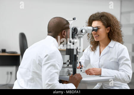 Photo of patient looking at medical apparatus during vision checking in ophthalmological laboratory with expirienced ophthalmologist..Trying to improve vision in modern oculist' cabinet. Stock Photo