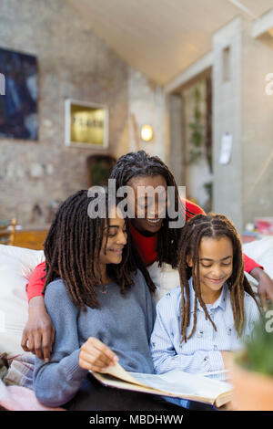 Smiling mother and daughters looking at photo album on sofa Stock Photo