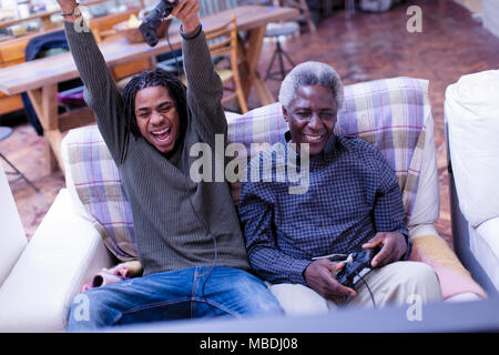 Enthusiastic grandfather and grandson playing video game on sofa Stock Photo