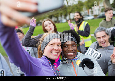 Smiling female runners with medal taking selfie at charity run in park Stock Photo