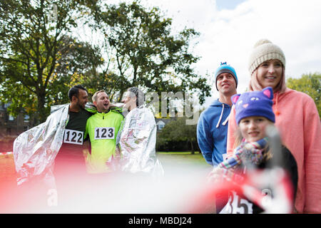 Male marathon runners wrapped in thermal blanket in park Stock Photo