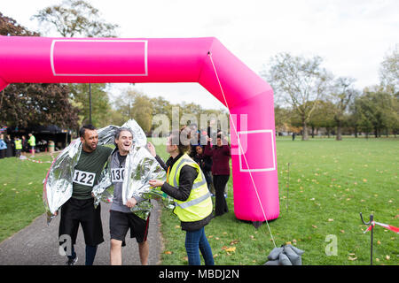 Volunteer wrapping male runners in thermal blanket at marathon finish line Stock Photo