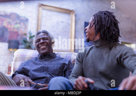 Grandfather and grandson laughing, playing video game on sofa Stock Photo