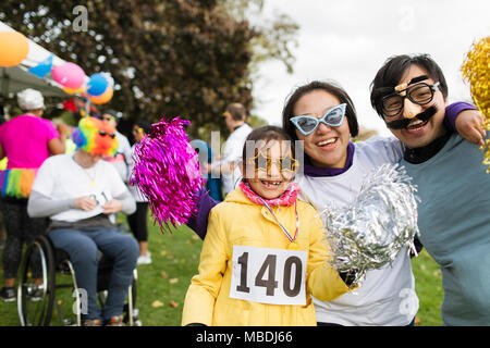 Portrait playful family wearing silly eyeglasses at charity run in park Stock Photo