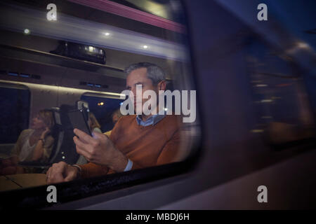 Businessman using smart phone at window on passenger train at night Stock Photo