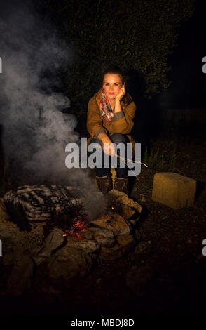 Into the wild. traveller woman sitting by a campfire Stock Photo