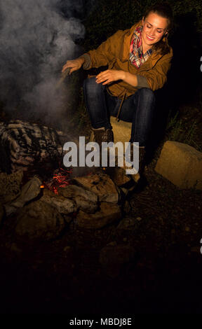 Into the wild. smiling healthy traveller woman sitting near a bonfire Stock Photo