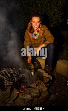 Into the wild. smiling healthy tourist woman near a bonfire roasting marshmallow Stock Photo