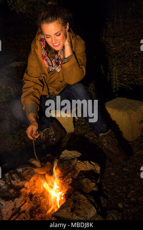 Into the wild. smiling healthy tourist woman by a bonfire grilling sausages Stock Photo