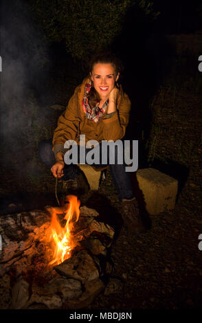Into the wild. Portrait of smiling tourist woman near a campfire grilling sausages Stock Photo