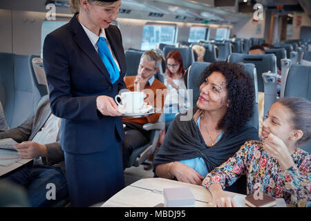 Attendant serving coffee to mother with daughter on passenger train Stock Photo