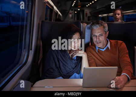 Couple using digital tablet on dark passenger train at night Stock Photo