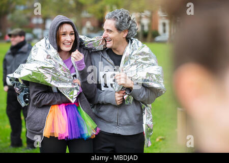 Happy couple runners wrapped in thermal blanket at charity run in park Stock Photo