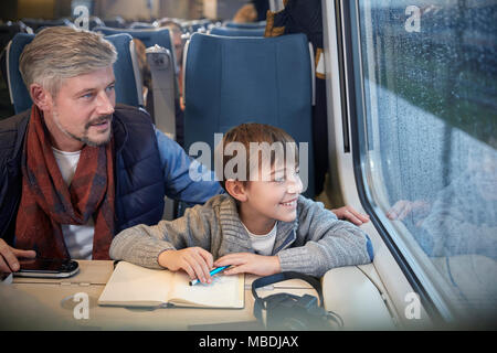 Father and son looking out window on passenger train Stock Photo