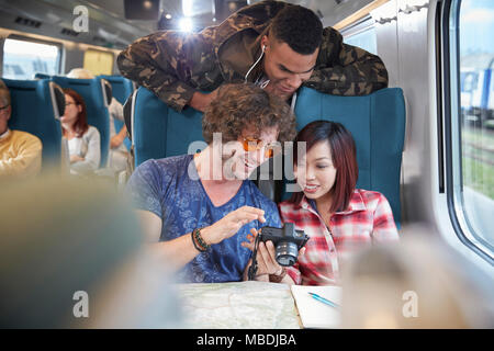 Young friends looking at photographs on digital camera on passenger train Stock Photo