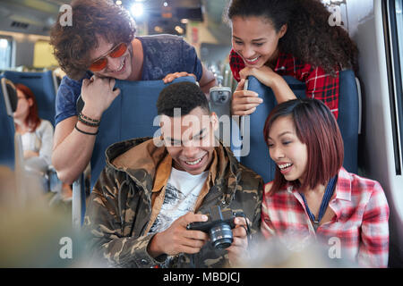 Young friends looking at photos on digital camera on passenger train Stock Photo