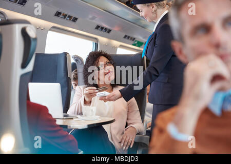 Woman with credit card using contactless payment, paying attendant on passenger train Stock Photo