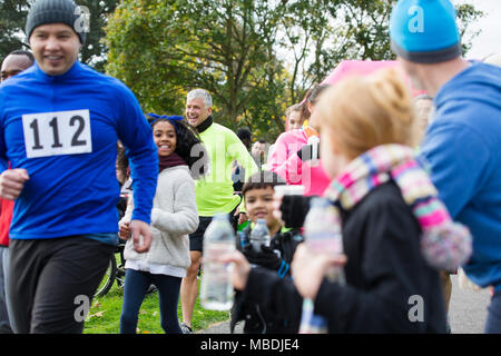 Spectators offering water to runners at charity run in park Stock Photo