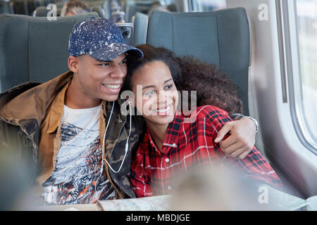 Affectionate young couple sharing headphones, listening to music and looking out window on passenger train Stock Photo