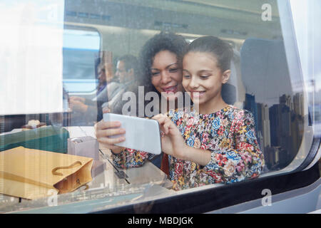 Mother and daughter using camera phone at window of passenger train Stock Photo