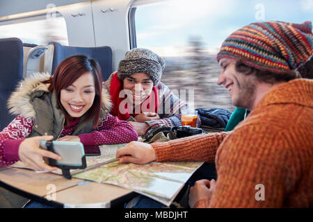 Young friends with map taking selfie with selfie stick on passenger train Stock Photo