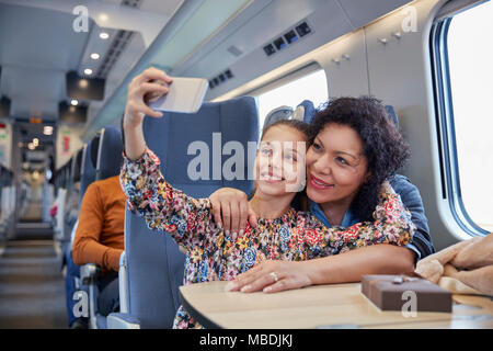 Affectionate mother and daughter taking selfie with camera phone on passenger train Stock Photo
