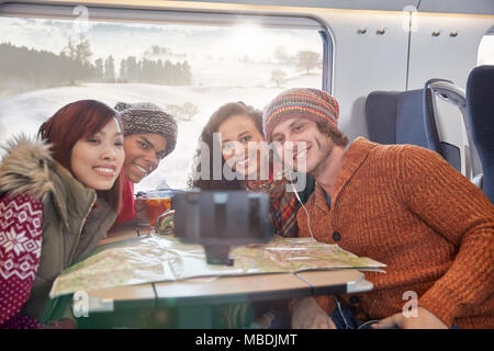 Happy young friends with map taking selfie with selfie stick on passenger train Stock Photo