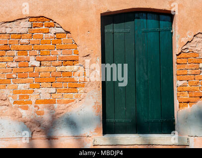 Window with green shutters on red brick wall of houses. Italy, Venice, Murano. Stock Photo