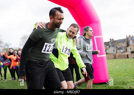 Man helping injured runner crossing finish line at charity run Stock Photo