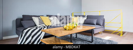 Citruses on wooden table next to a corner couch with yellow pillow and striped blanket in living room interior Stock Photo