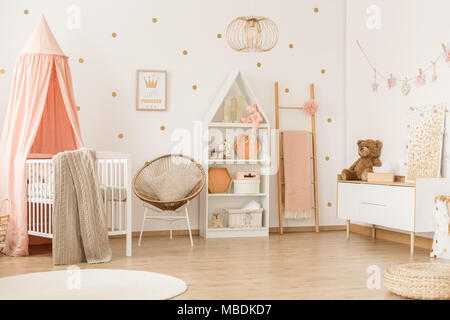 Teddy bear on white cupboard in scandi child's bedroom interior with canopied crib