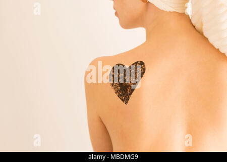 Close up woman with coffee scrub in a heart shape on her back and shoulder. Skin care concept, exfoliation Stock Photo