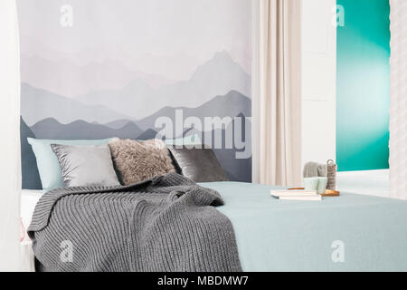 Grey blanket and books on bed in simple bedroom interior with mountain wallpaper