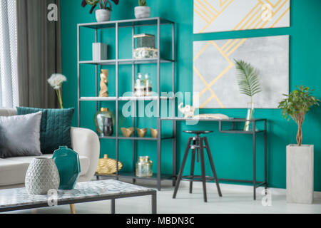 Black chair at desk against green wall with gold posters in living room interior with vases Stock Photo