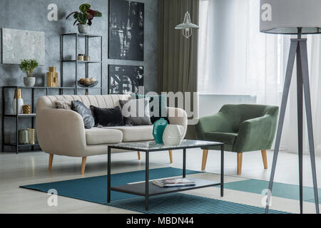 Lamp in elegant living room interior with green armchair next to a sofa and table Stock Photo