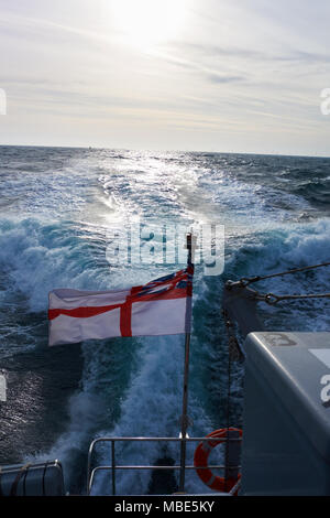 A British White Ensign flying from the back of Royal Navy P2000 HMS Dasher P280 in the sunlight Stock Photo