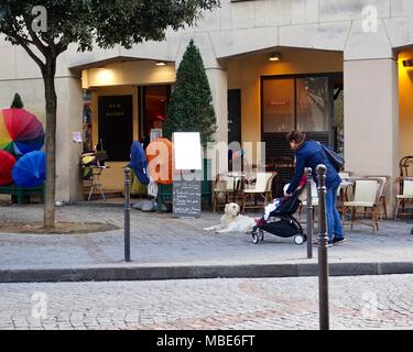 Mother and child, in stroller, stop to admire a sweet dog in front of a cafe, not yet open for the day. Paris, France. Stock Photo