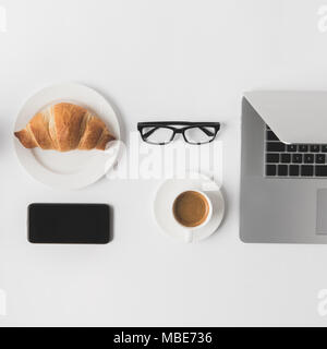 flat lay with digital devices, eyeglasses and breakfast on white tabletop Stock Photo