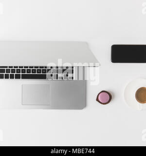 flat lay with laptop, smartphone, cup of coffee and dessert on white tabletop Stock Photo