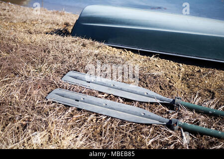 Small dinghy with two metal oars lying on dried grass on a river or lake bank ready to go rowing in a close up view Stock Photo