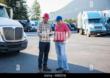 Truck driver team of caucasian drivers going over dispatch information in the parking lot of a truck stop. Stock Photo