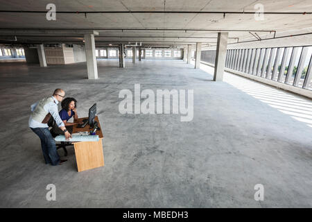 Black business woman and Asian business man working on a computer at a desk in a large new empty office space. Stock Photo