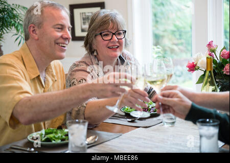Senior couples toasting a home dinner party with glasses of white wine. Stock Photo